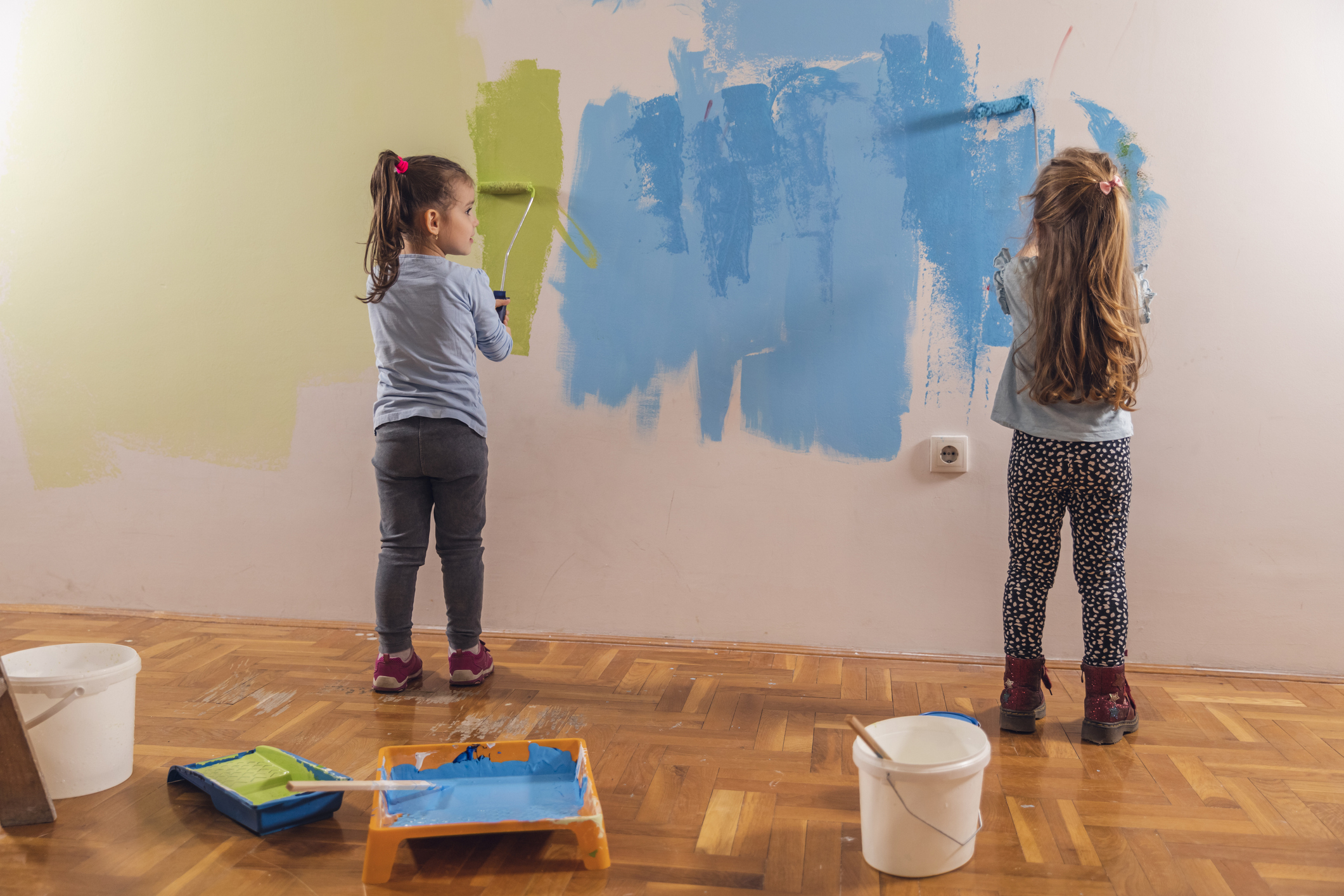 Zwei kleine Kinder streichen gemeinsam eine Wand.
