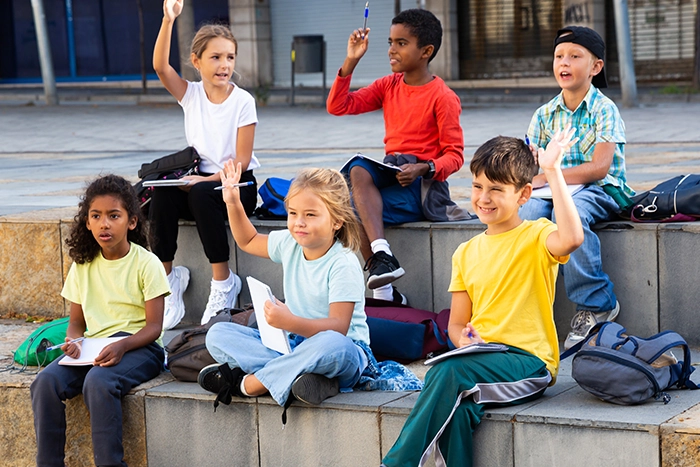 Sechs Schüler sitzen auf Stufen auf dem Pausenhof. Vier von ihnen haben die Hand erhoben